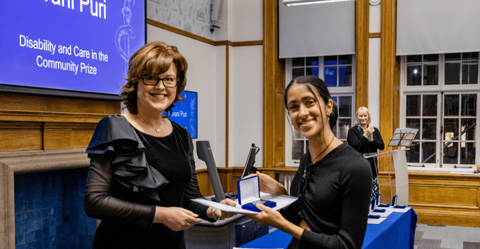 a woman presents another woman with a certificate and medal