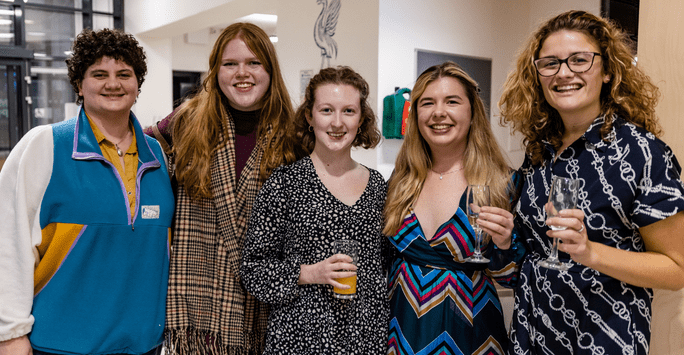 a group of women pose for the camera, raising their glasses in celebration