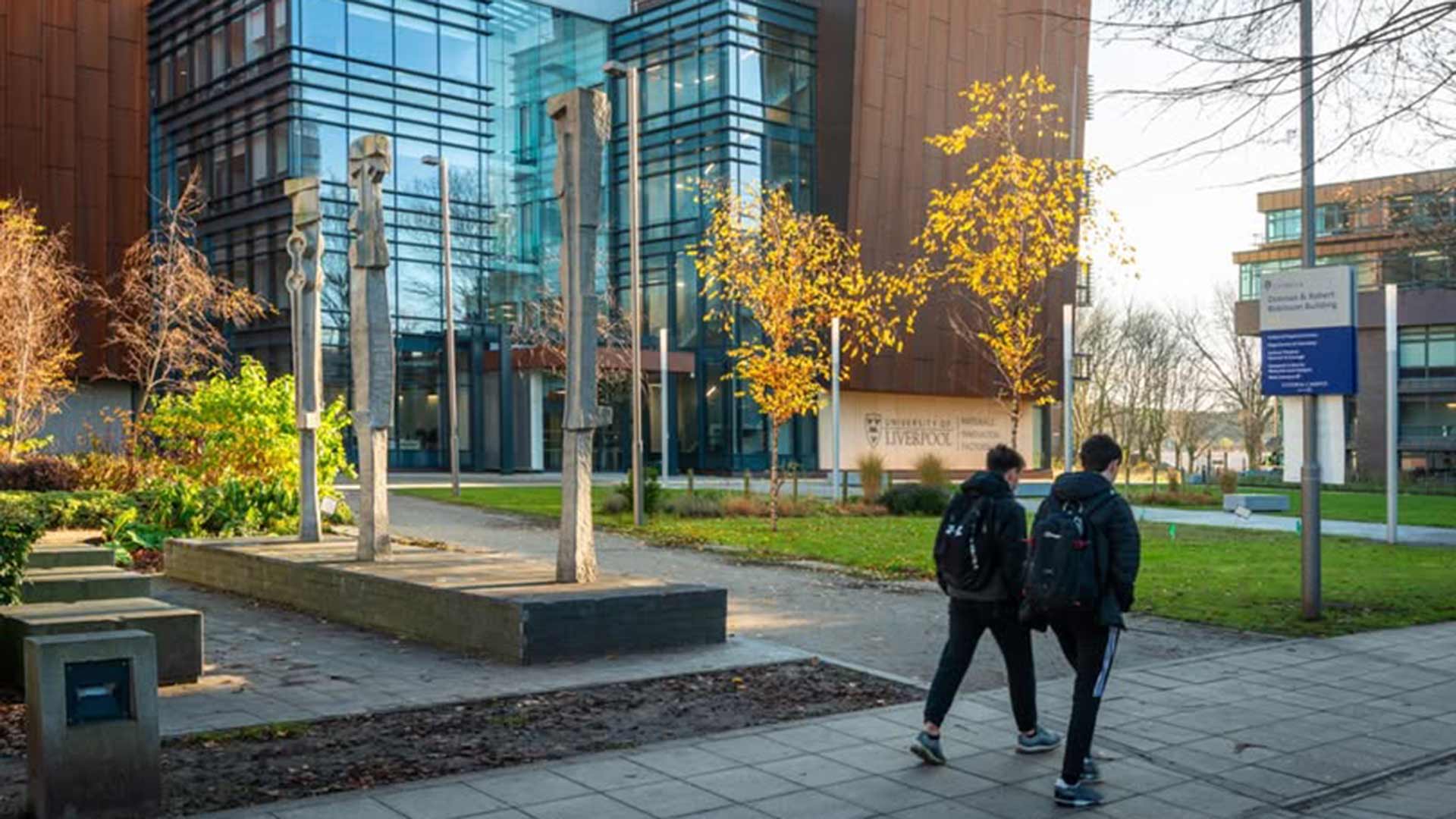 students walk across university campus with a glass building and yellow leafed trees in the background