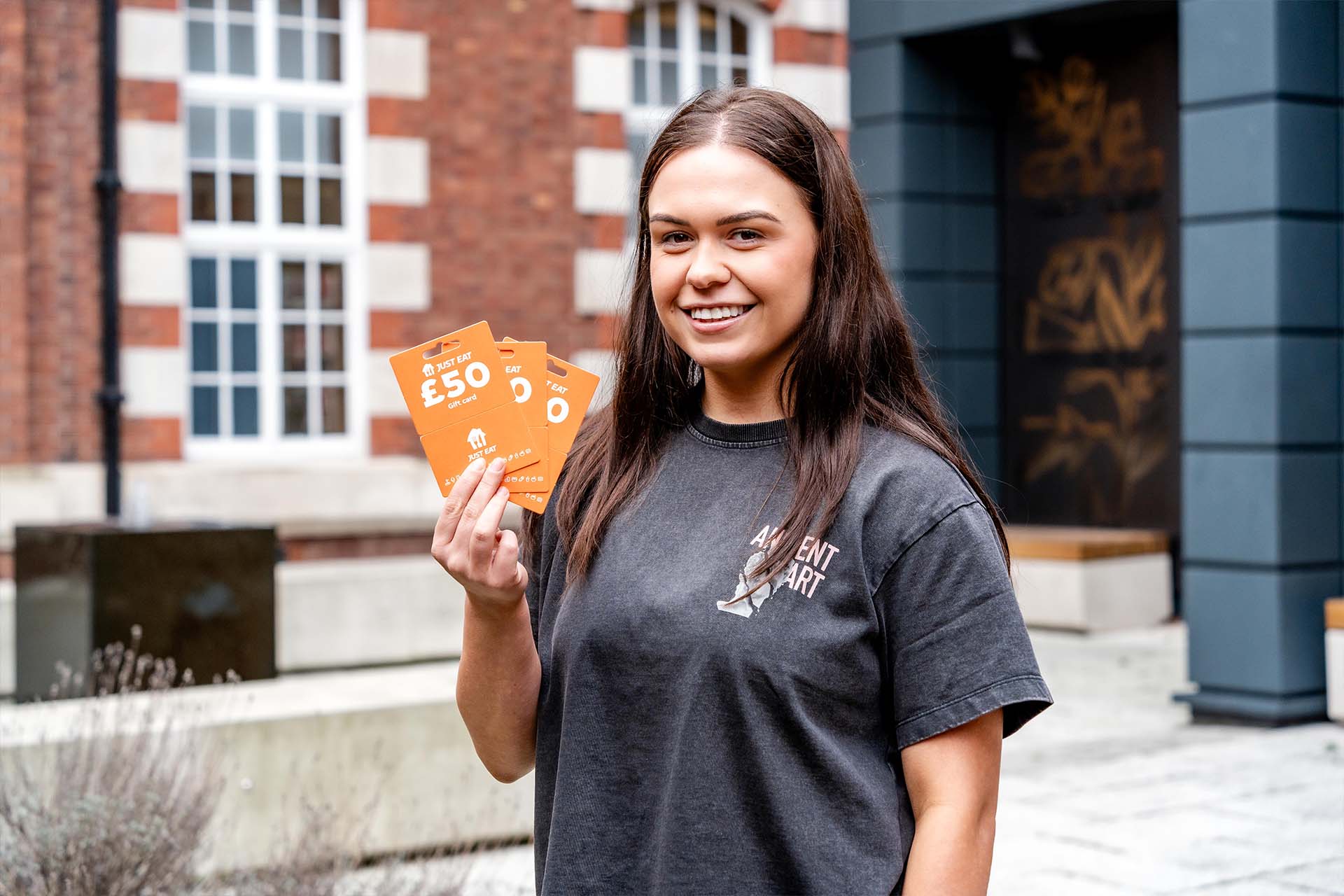 A headshot of student doctor Taia Rothwell holding three Just Eat vouchers. She has brown hair and is wearing a grey t shirt.