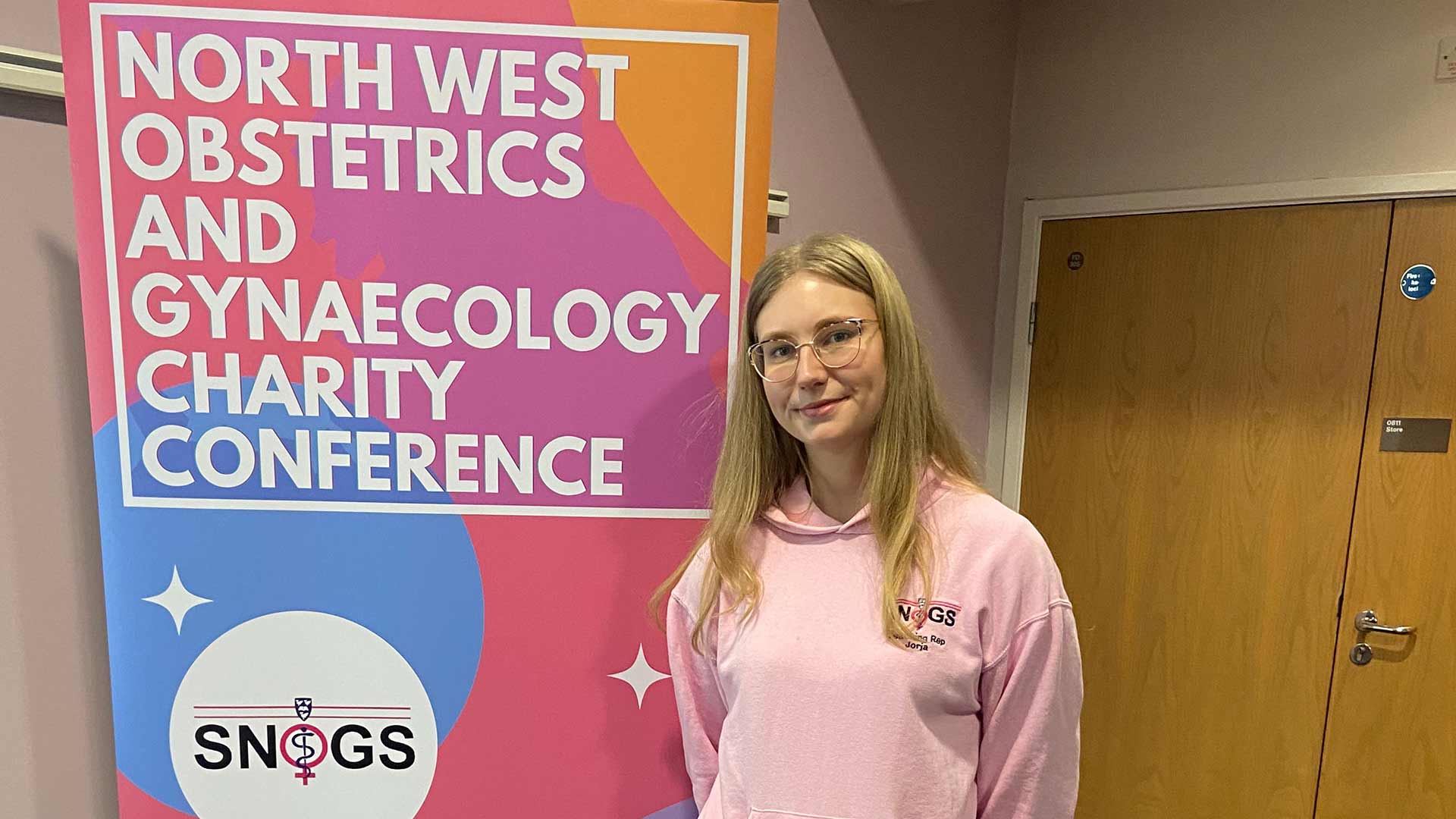 student standing alongside banner that read north west obstetrics and gynaecology charity conference