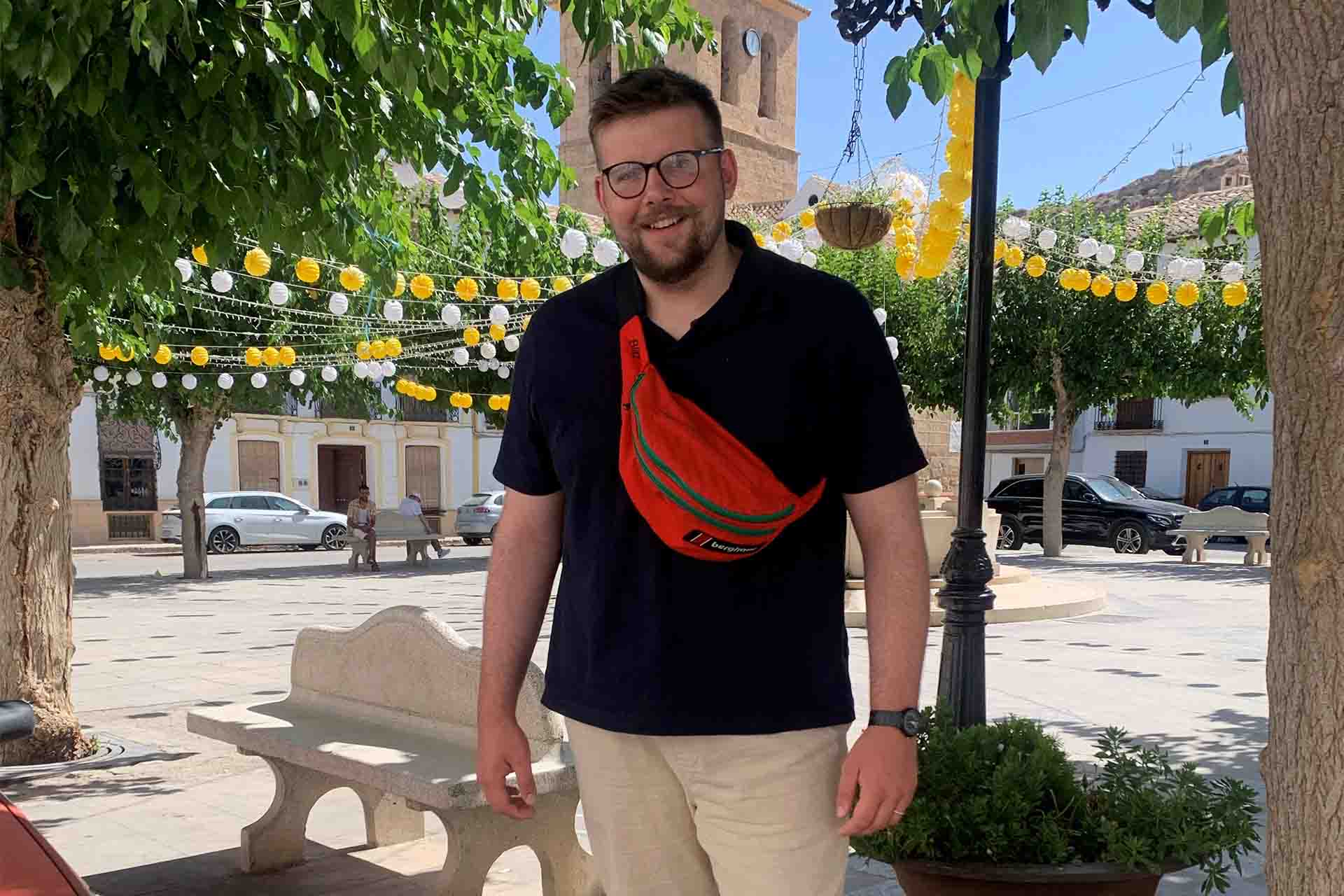 a man in a european square with blue skies and green trees