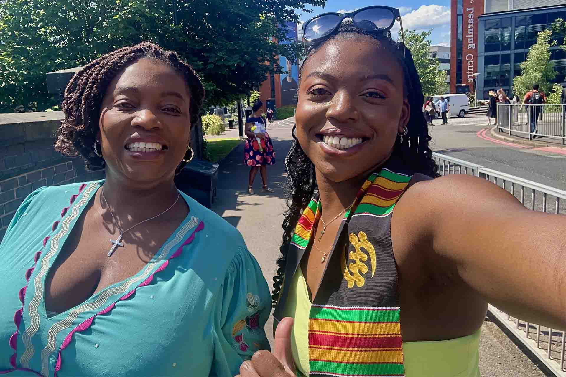 two women in bright colours smiling with green trees and blue skies