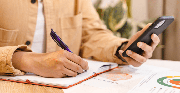 close up of a person making notes and using a phone