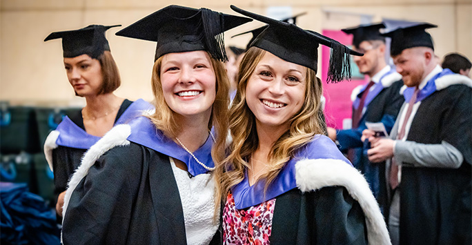 Two students smiling in caps and gowns for graduation