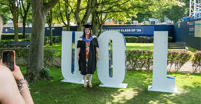 Graduate posing by the UoL sign