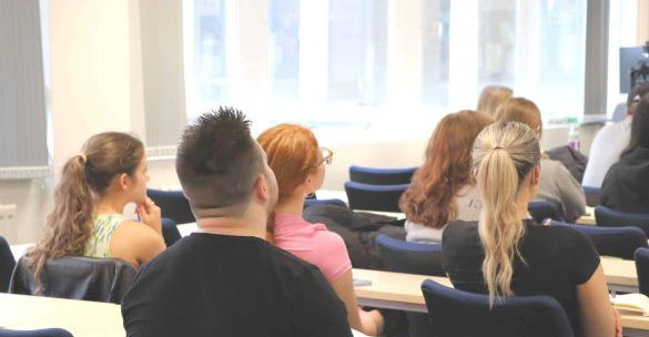 Students sit behind tables in a seminar room