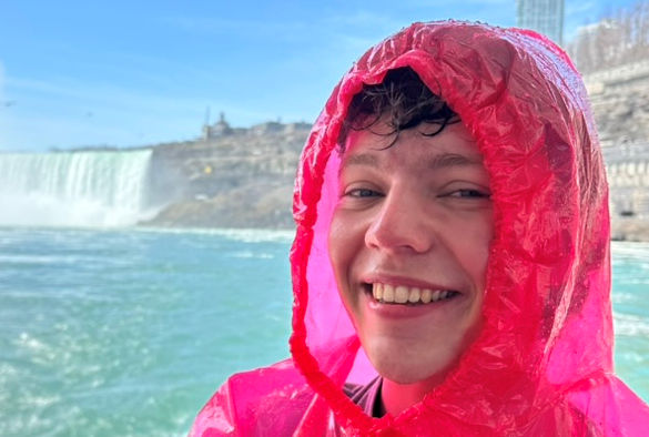 A student wears a pink rain poncho in front of a waterfall