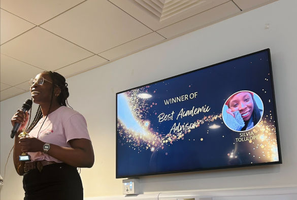 Silvia Tolulope stands in front of a screen holding an award