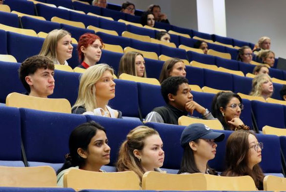 Students sit in rows of blue seats in a lecture theatre