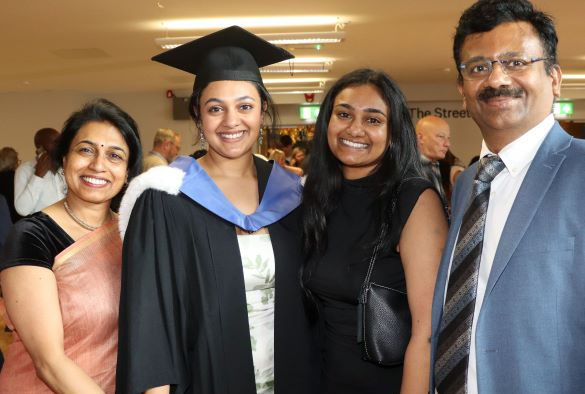 A student wearing a blue and black gown smiles as she stands with her family and friends