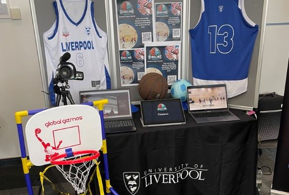 A display table covered in a black cloth underneath signs and basketball shirts