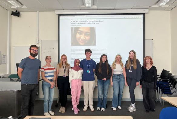 Students and supervisors stand in front of a projection screen