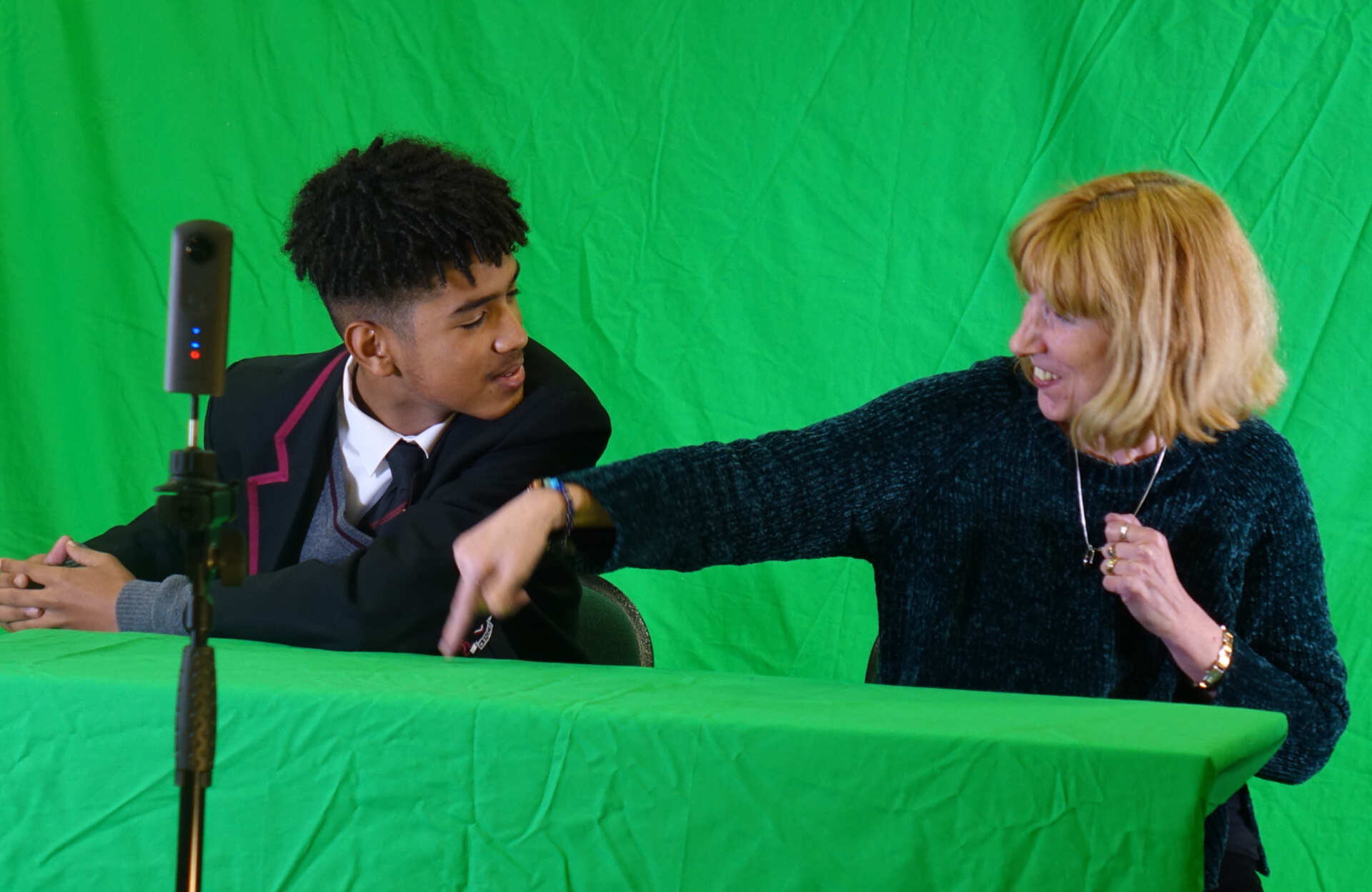 School pupil and adult sat in front of a green screen