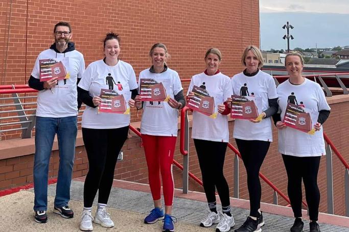 The brave staff who took part in the Anfield Abseil pose near the stand wall with their certificates