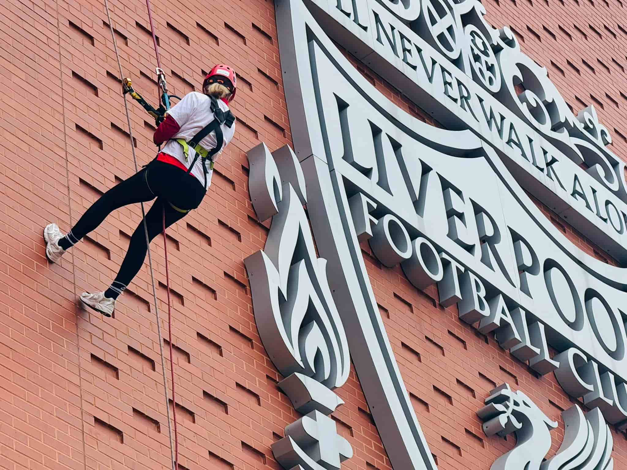 Carla abseiling down the main stand at Anfield with the Liverpool FC logo visible beside here