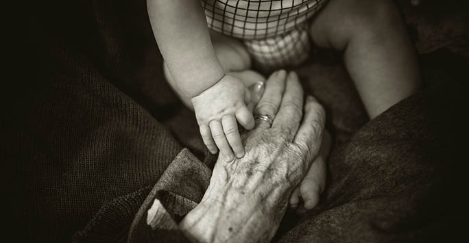 Older person and baby holding hands.