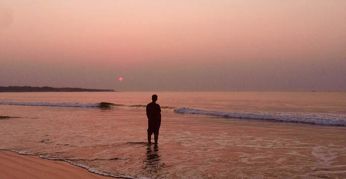 A person stood alone on a beach at sunset.