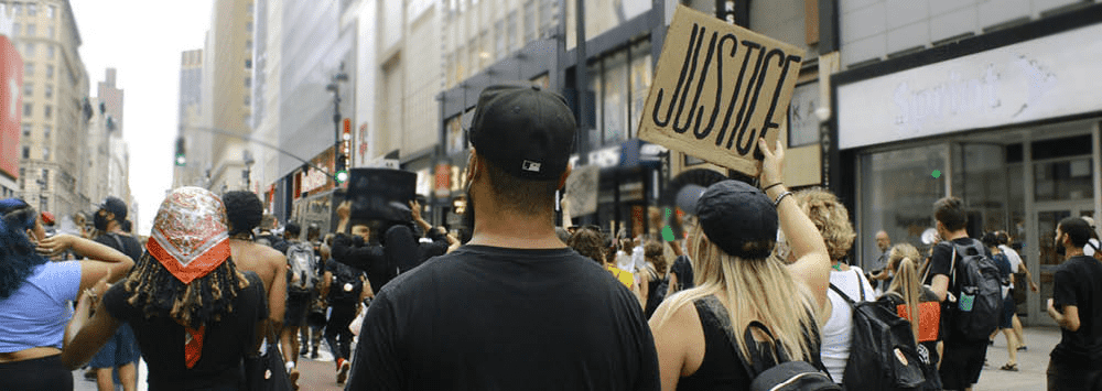 A crowd of people walking through the street holding up a sign that reads 'Justice'.