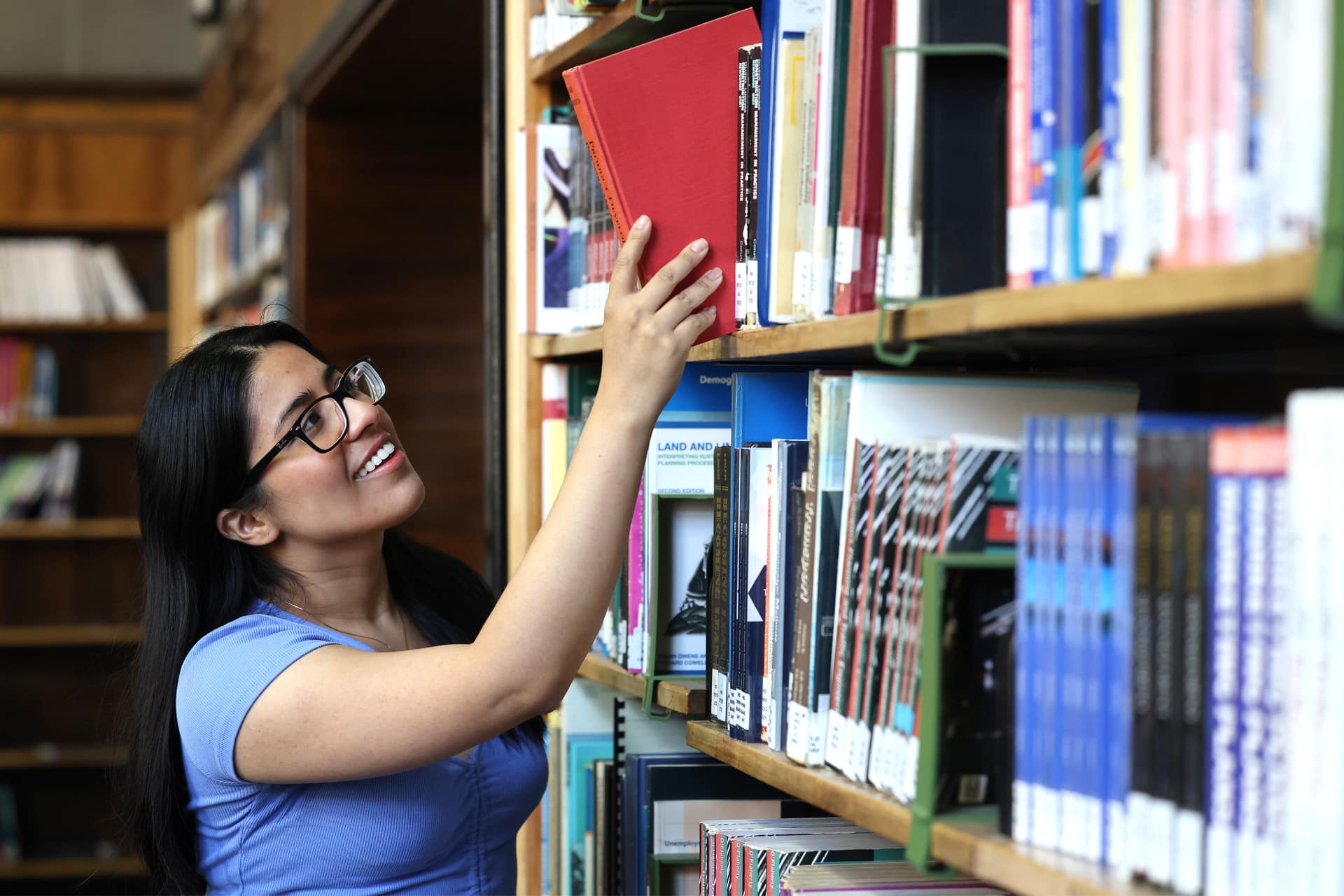 A students pulls a book from a bookshelf filled with books.