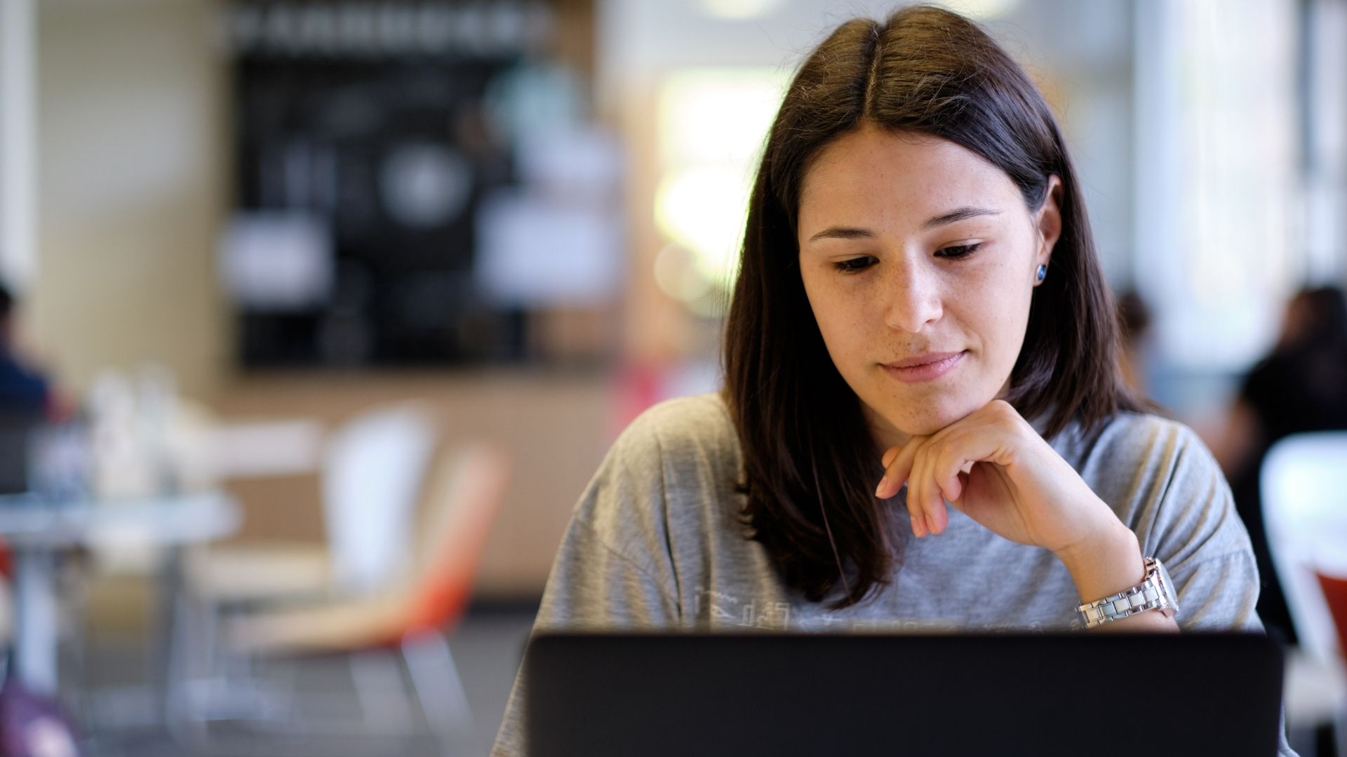 An image of a young woman in front of a laptop screen looking hopeful.