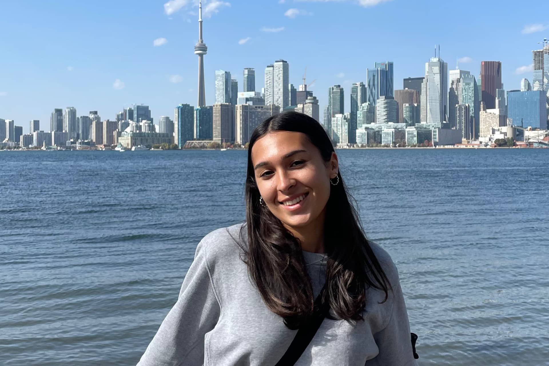 Riya standing in front of water with a city in the background