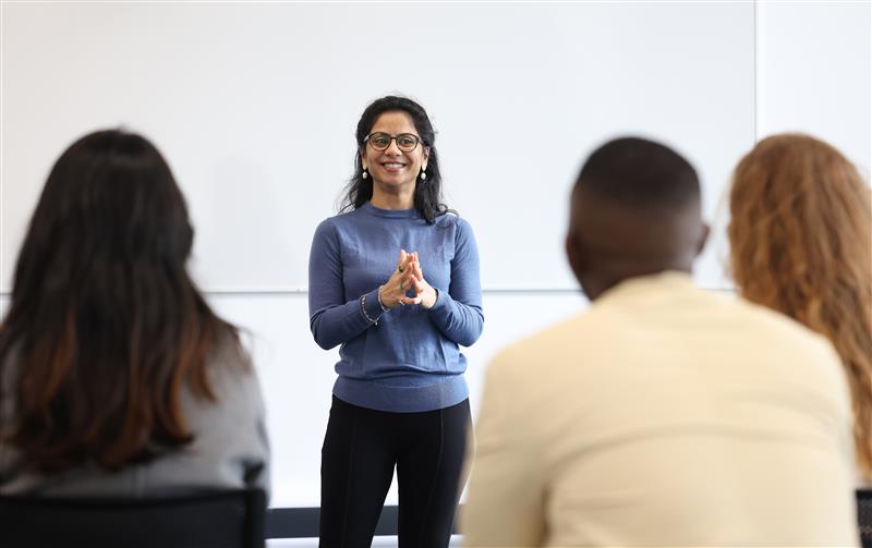 A female student stands at the front of a classroom, teaching.