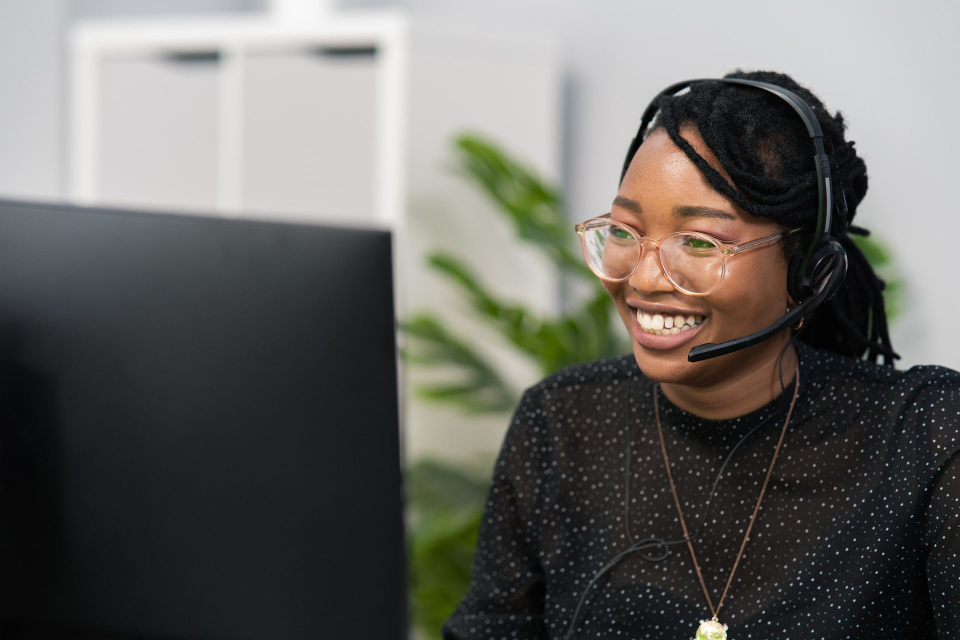 A woman smiling and wearing a headset in front of a computer.