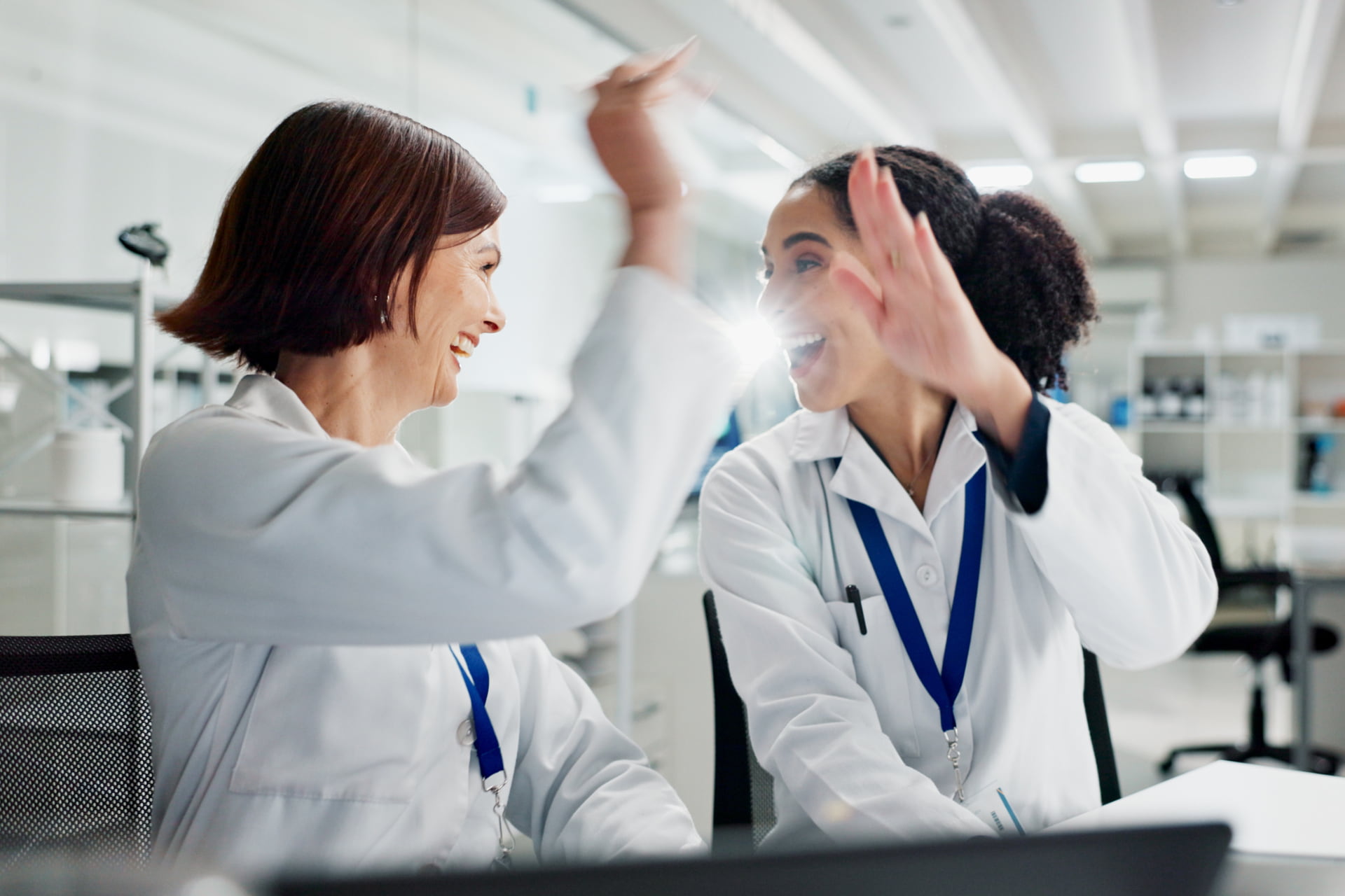 Two women high fiving at a laptop in lab celebrating.