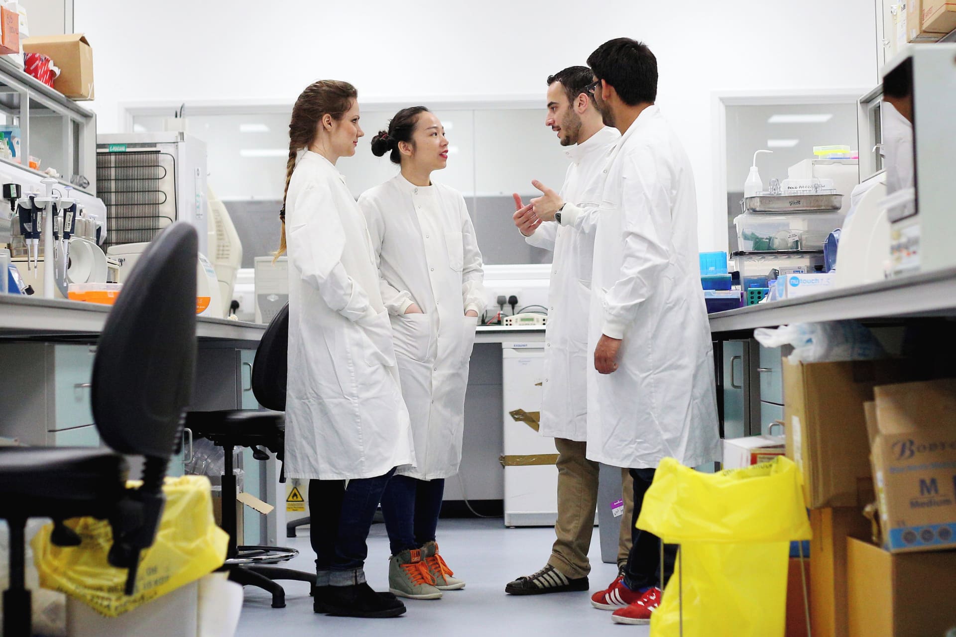 Group of people wearing lab coats standing and talking in a lab.