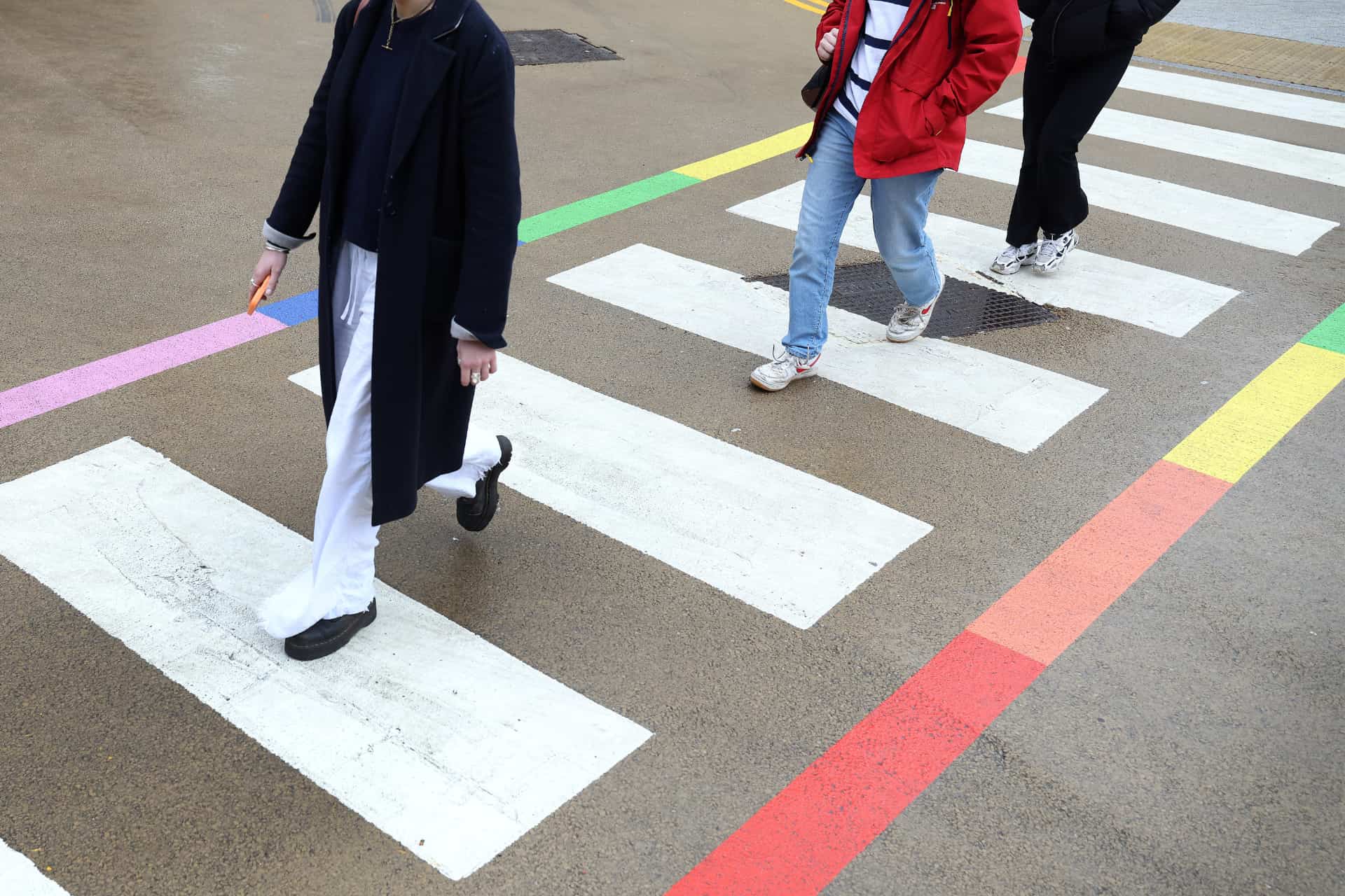 Three people walking across a crosswalk with rainbow colouring on the sides.