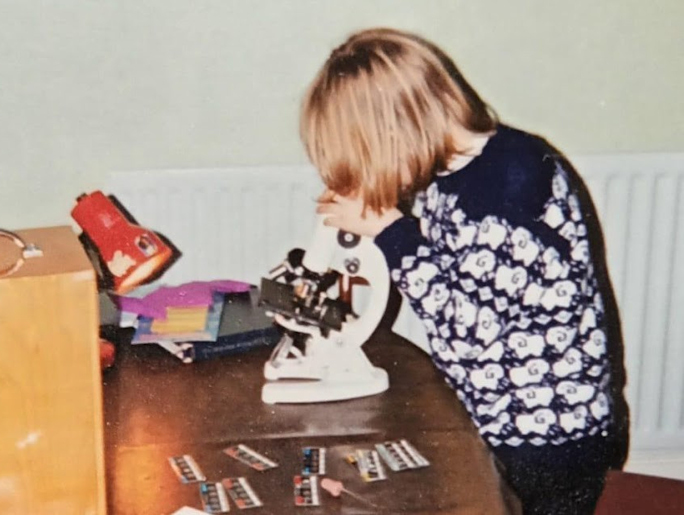 Elinor as a child playing with a microscope on a dining table
