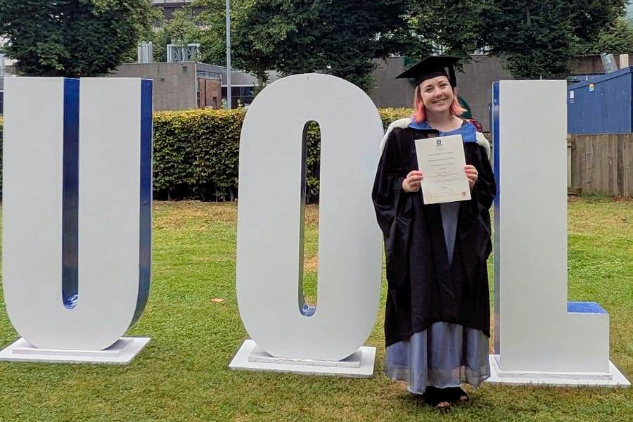 A photo of Jemma Clarke on graduation robe in front of large UOL sign letters