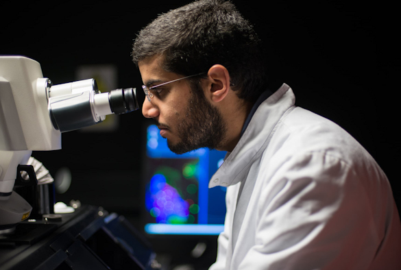 A male in a white lab coat looking into a microscope