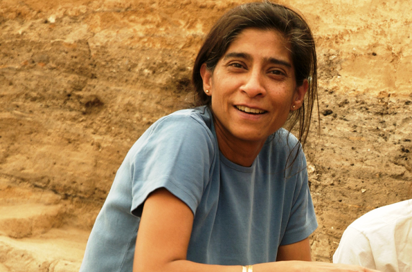 A person on an Archaeological site crouching in front of a rock