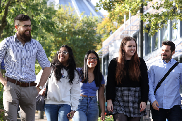 Five students walking outside in a line smiling with each other 